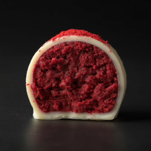 Close-up af en hvid chokoladetrøffel skåret midt over, der viser den bløde fyldige red-velvet kage som kerne.